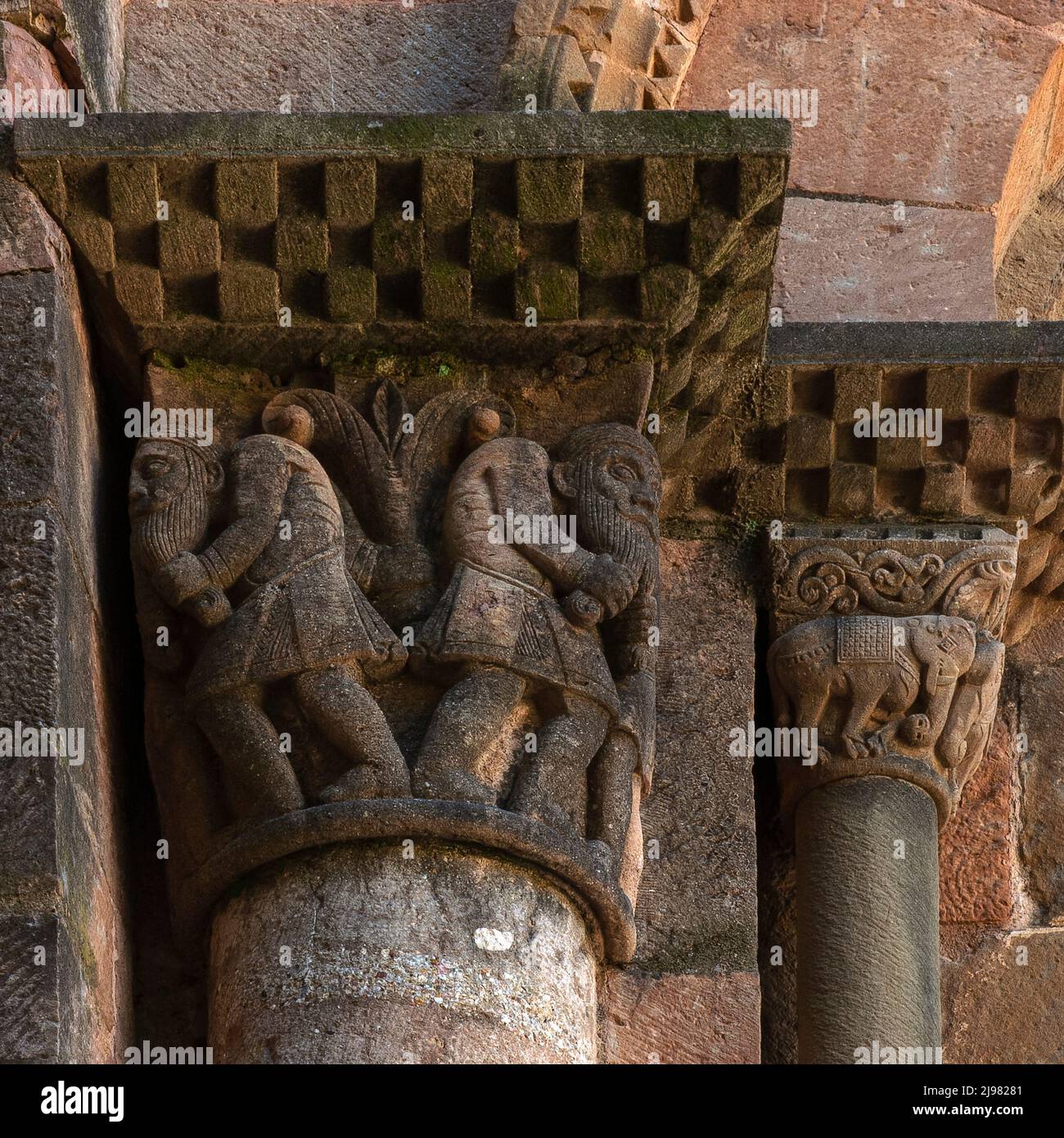 Pair of Langobardi men tugging at their long beards and elephants standing head-to-head.  Sculpted capitals in Italian Lombard Romanesque style on the outside of the apse of the 1100s AD monastery church at Sant Joan de les Abadesses in Ripollès county, Catalonia, Spain. Stock Photo