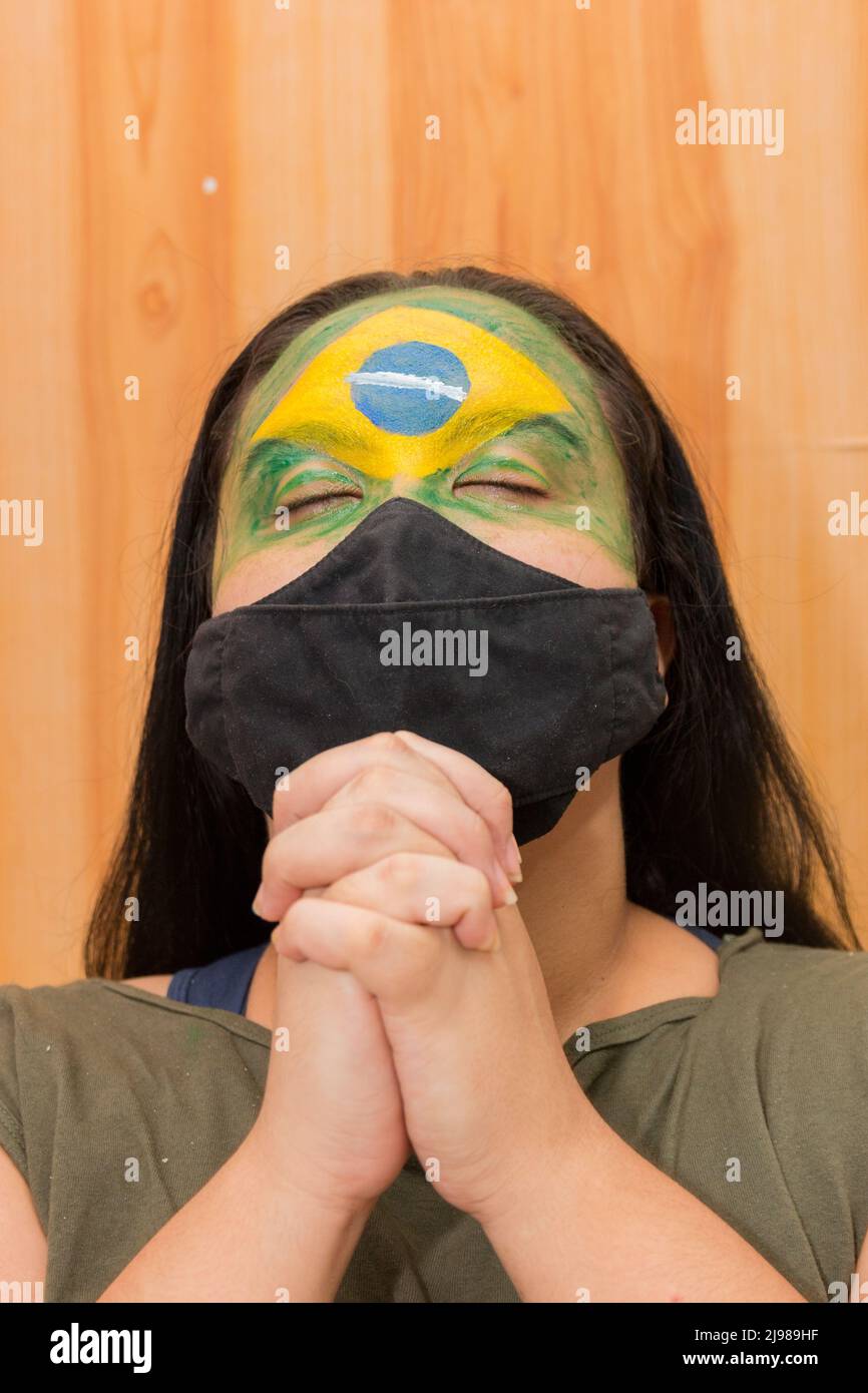 Woman with the flag of Brazil painted on her face with a black mask in Rio de Janeiro. Stock Photo