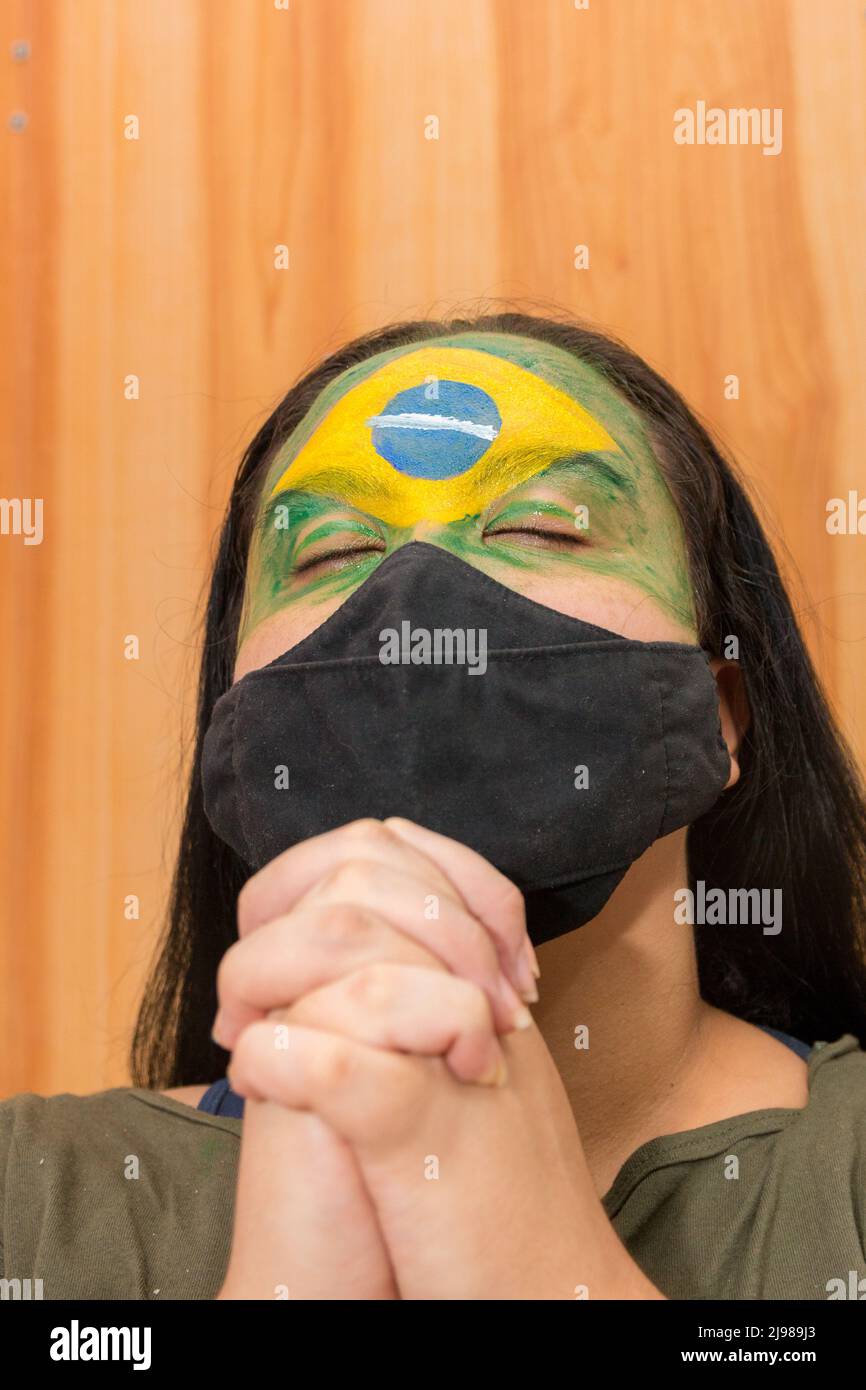 Woman with the flag of Brazil painted on her face with a black mask in Rio de Janeiro. Stock Photo