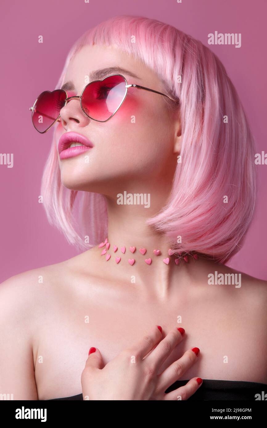 Close-up portrait of woman in sunglasses with bright colored pink hair and make-up on pink. Professional coloring Stock Photo