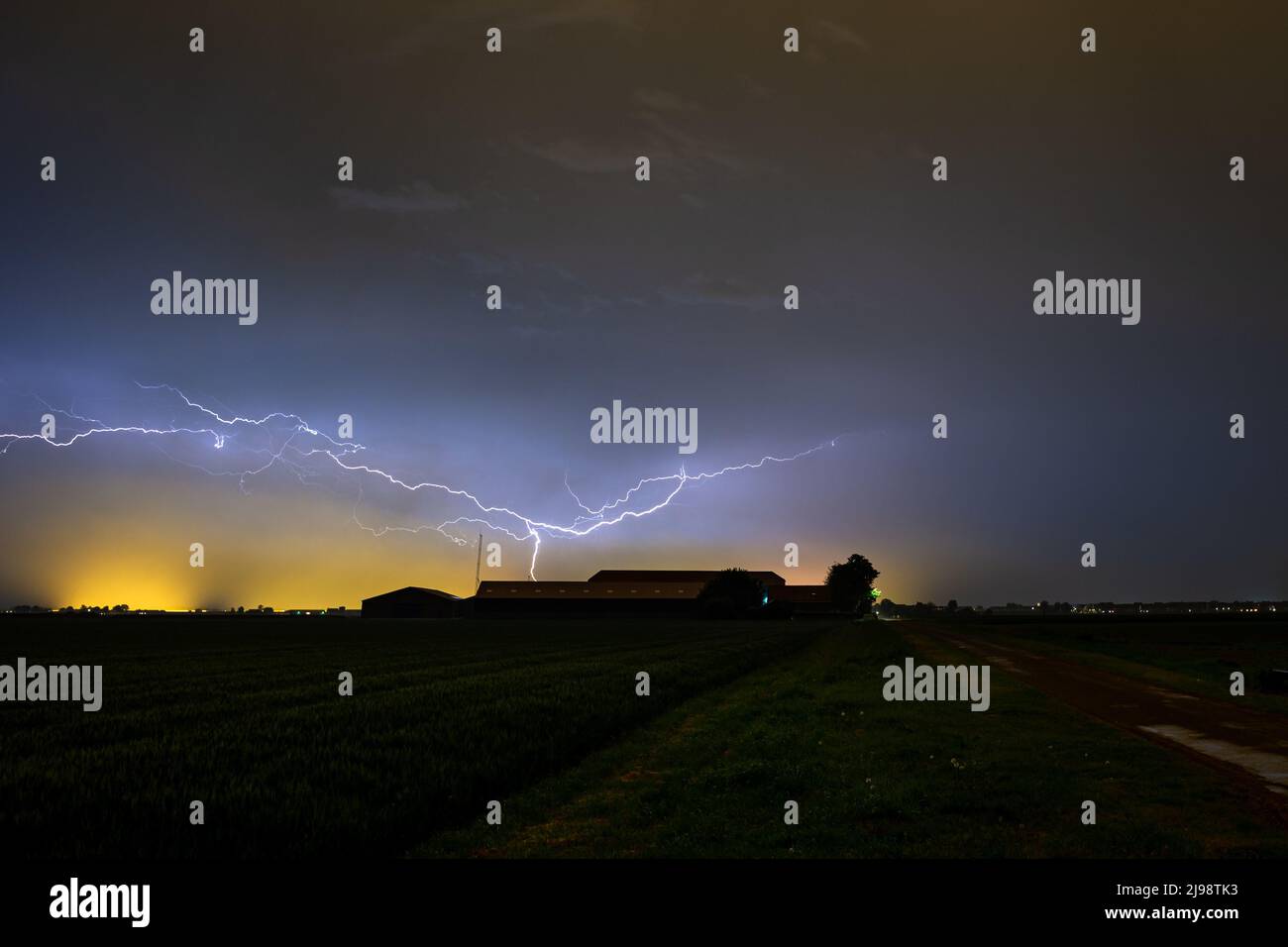 Dramatic image of lightning cleaving the sky above a farm during a thundery night in May. Stock Photo