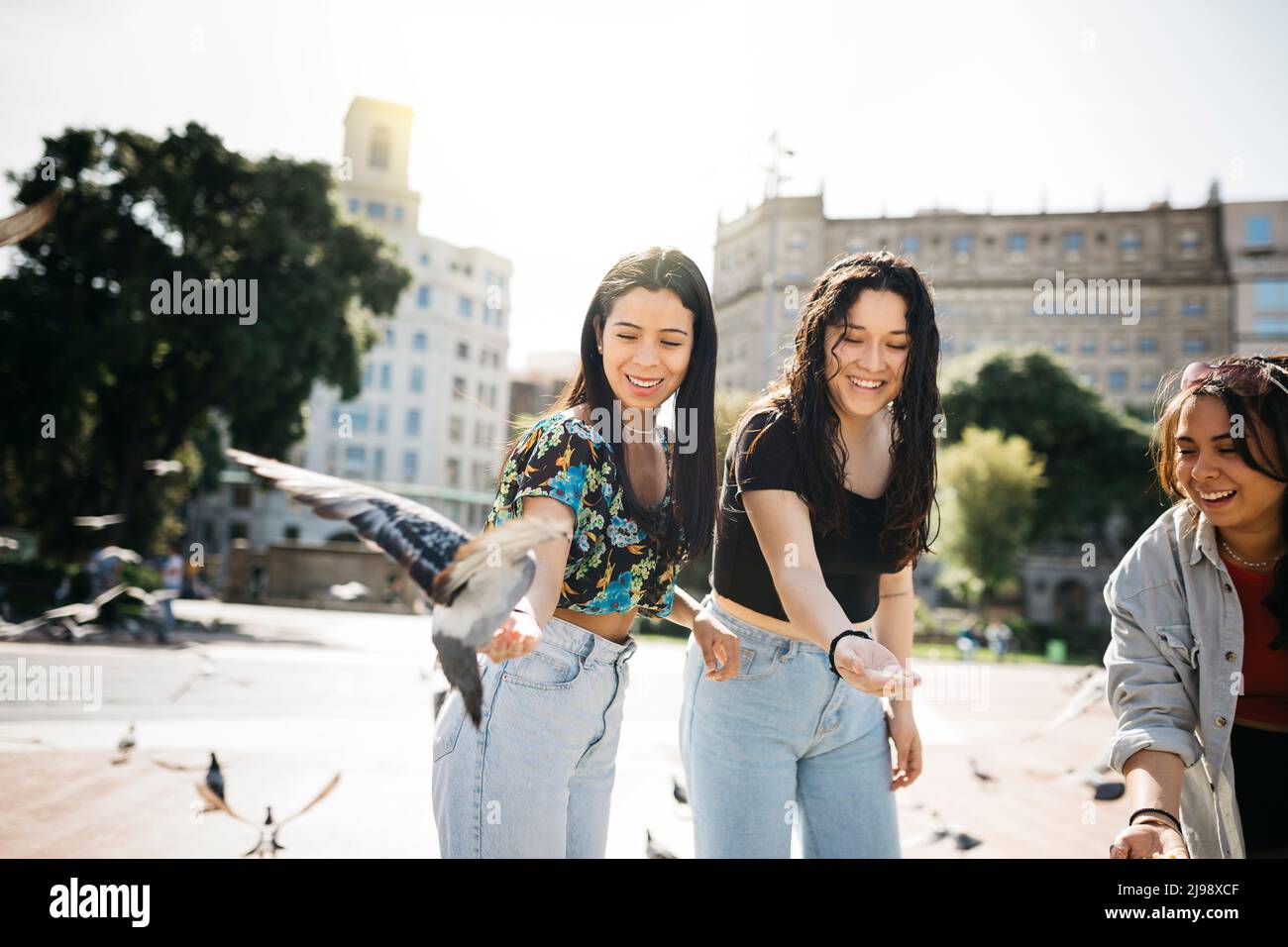 Three young women feeding pigeons in a square of a city Stock Photo