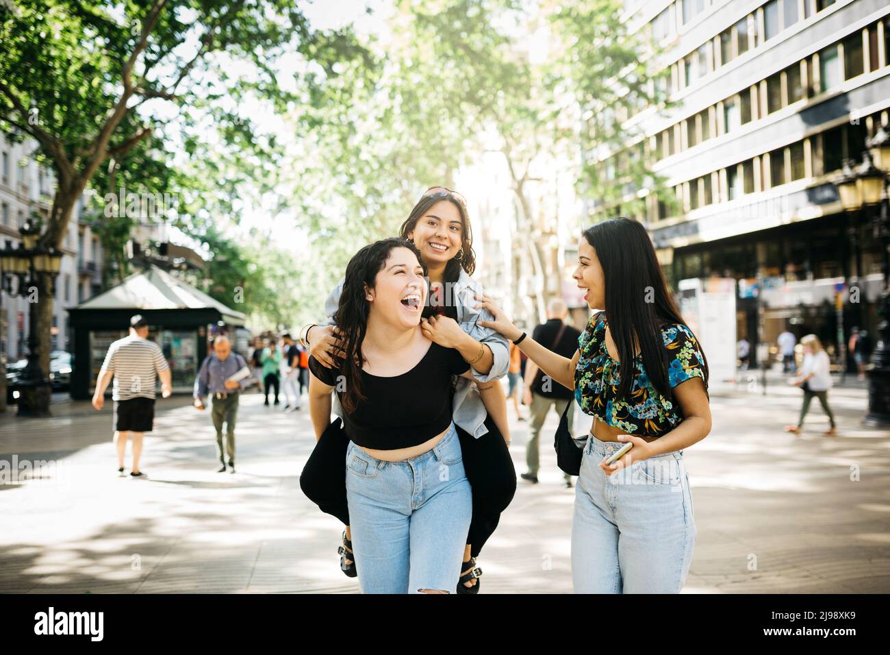 Young women piggybacking a friend while walking down Las Ramblas of Barcelona Stock Photo