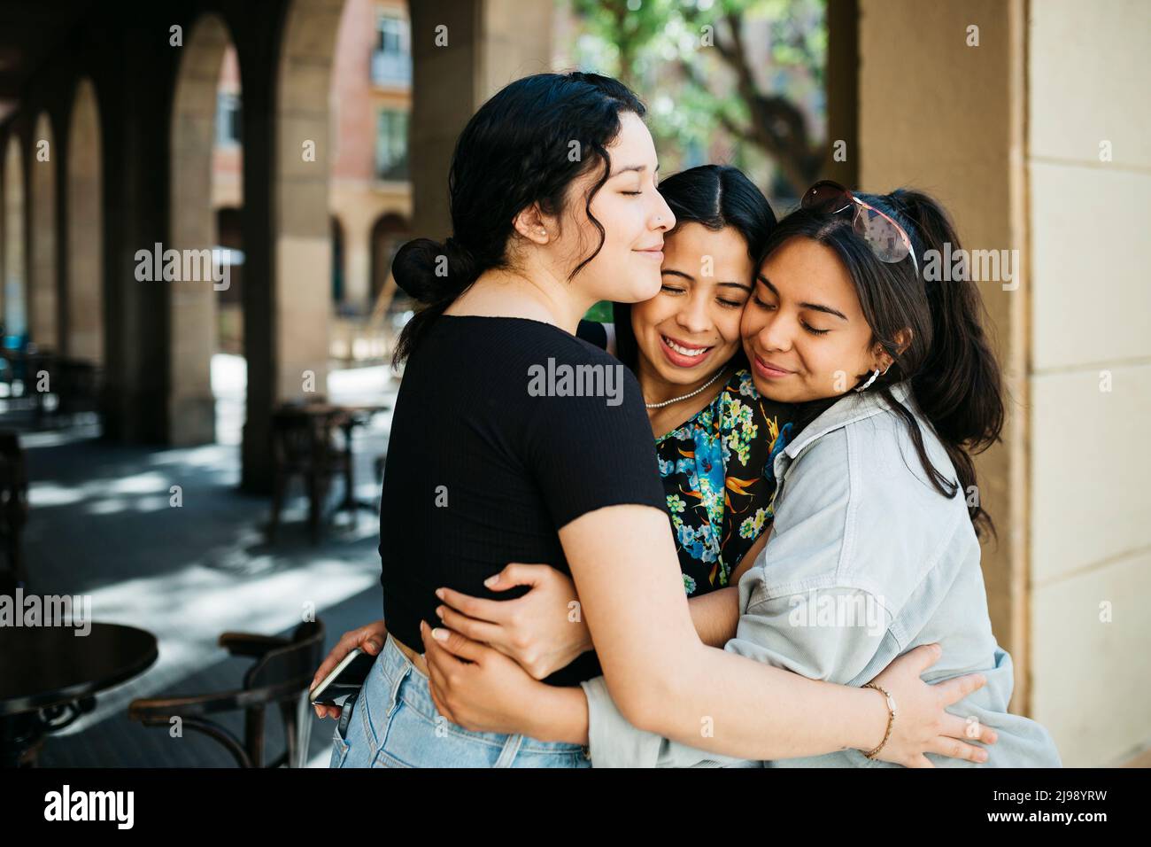 Three young latin american women embracing on the street Stock Photo