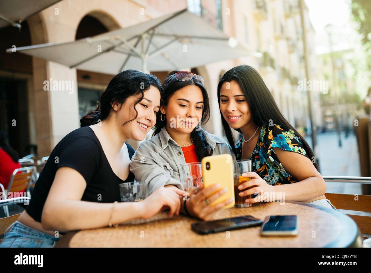 Three young women taking a selfie with a phone on terrace of a restaurant Stock Photo