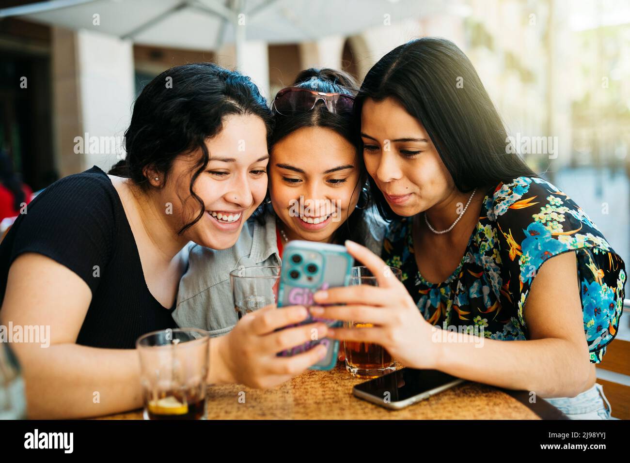 Three young women looking at a phone on terrace of a restaurant Stock Photo