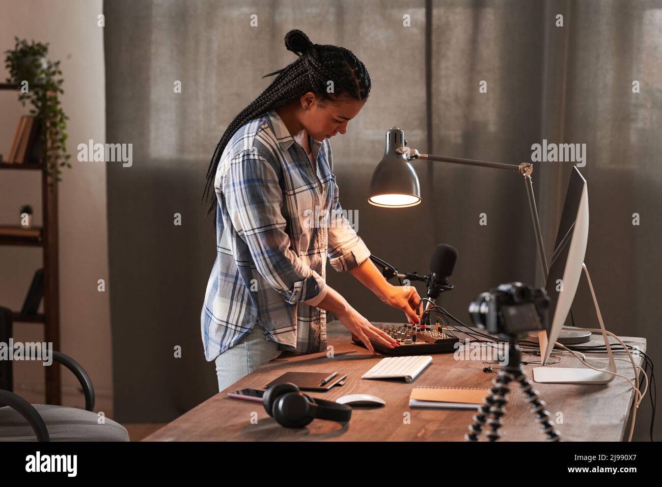 Stylish young woman standing at table in loft home office room setting and turning on microphone preparing for vlogging Stock Photo