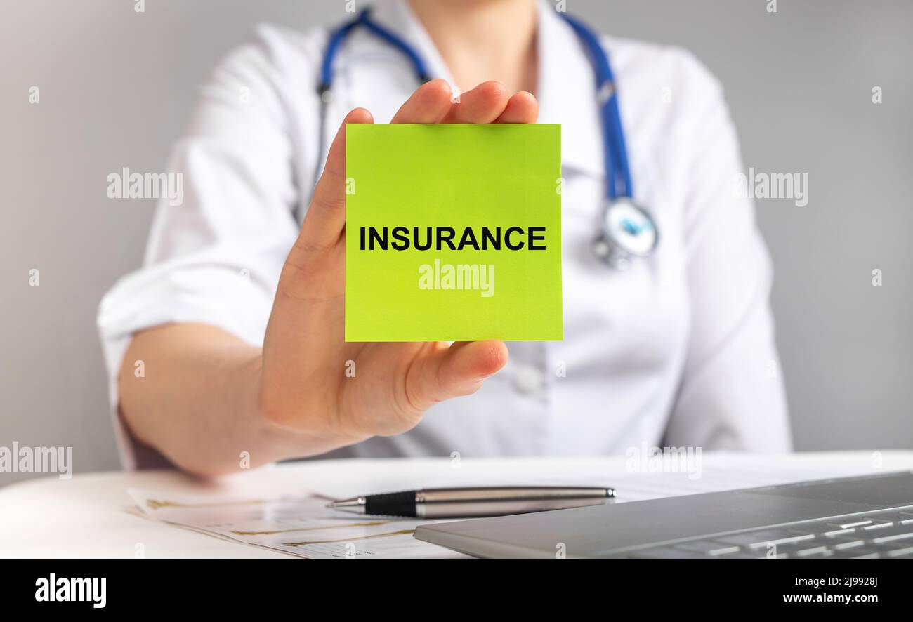 Medical insurance concept. Doctor with stethoscope sitting at table with laptop and holding paper with text. Payment of health care costs, medicine expenses. High quality photo Stock Photo