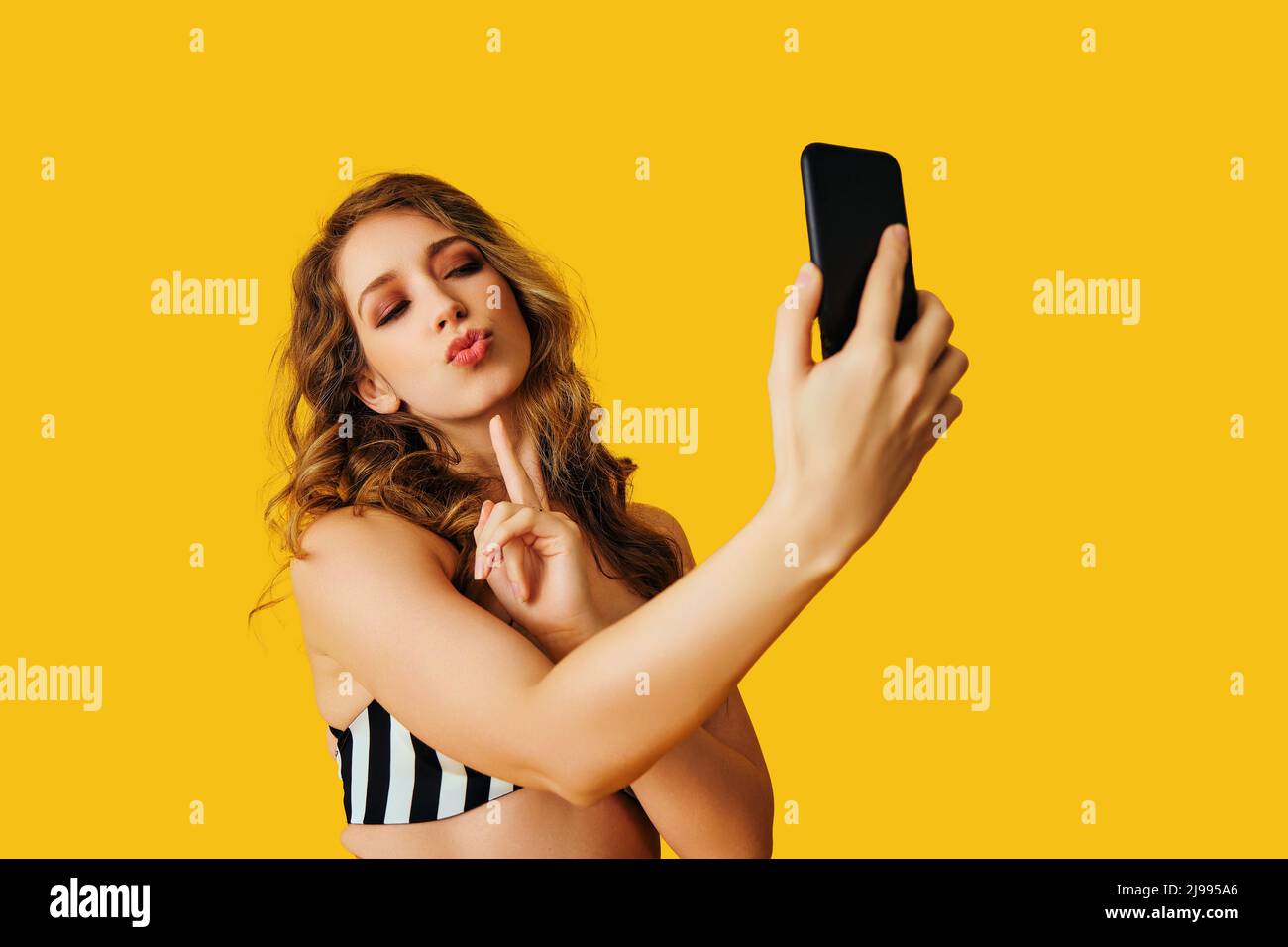 portrait of beautiful young woman texting flirt selfie photo message with smartphone on yellow background studio Stock Photo