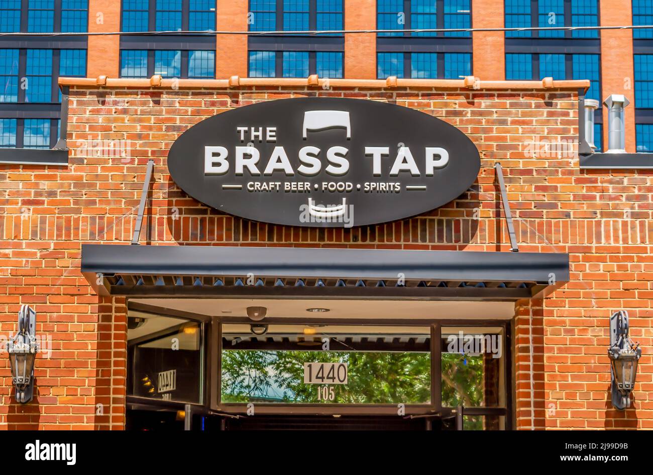Horizontal, medium shot of 'The Brass Tap' craft beer tap room's exterior facade brand and logo signage below reflective windows and above entrance. Stock Photo