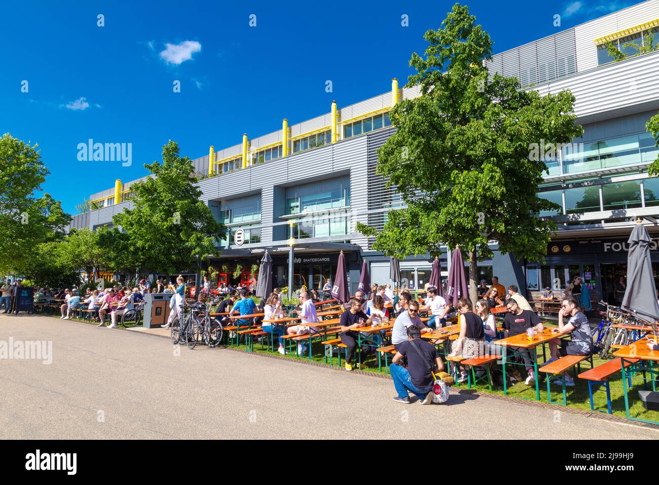 People relaxing at restaurants in Here East on a sunny day along the River Lee Navigation canal, Olympic Park, Stratford, London, UK Stock Photo