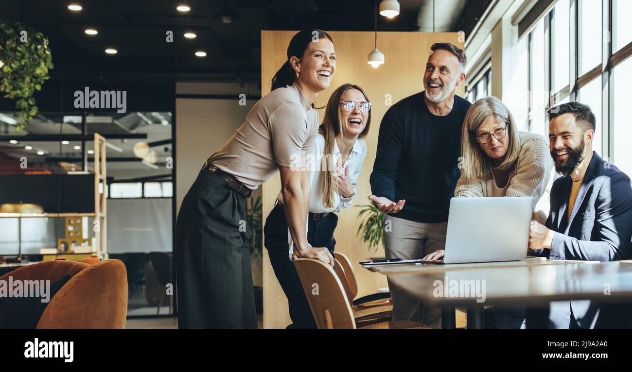 Happy businesspeople laughing while collaborating on a new project in an office. Group of diverse businesspeople using a laptop while working together Stock Photo