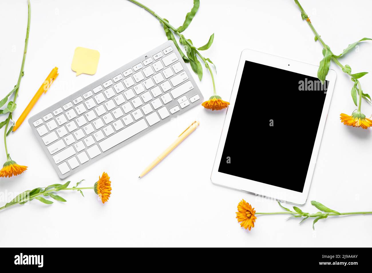 Tablet with computer keyboard, pens, sticky note and flowers on white background Stock Photo