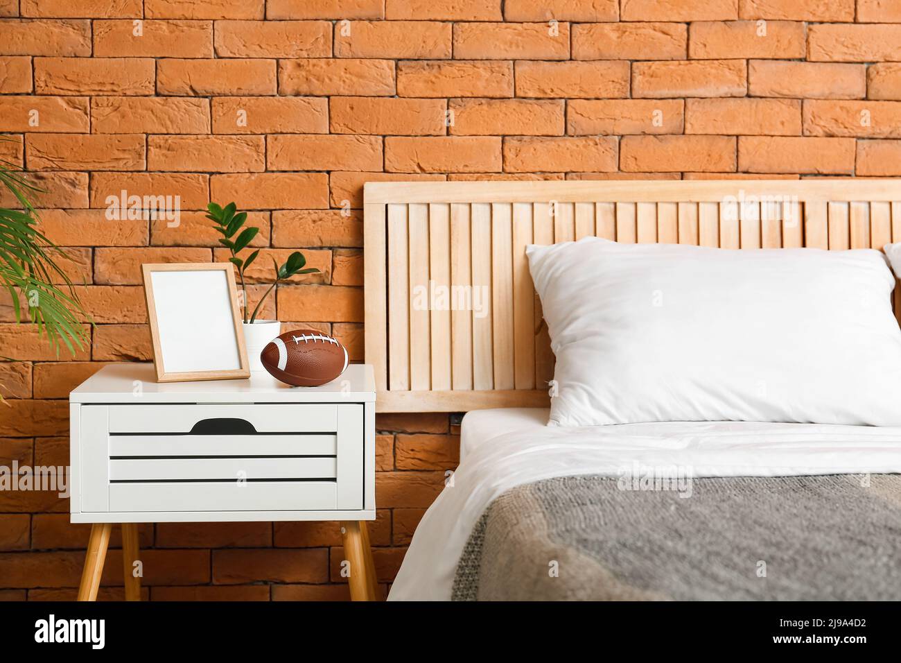 Rugby ball and blank photo frame on nightstand near brick wall in