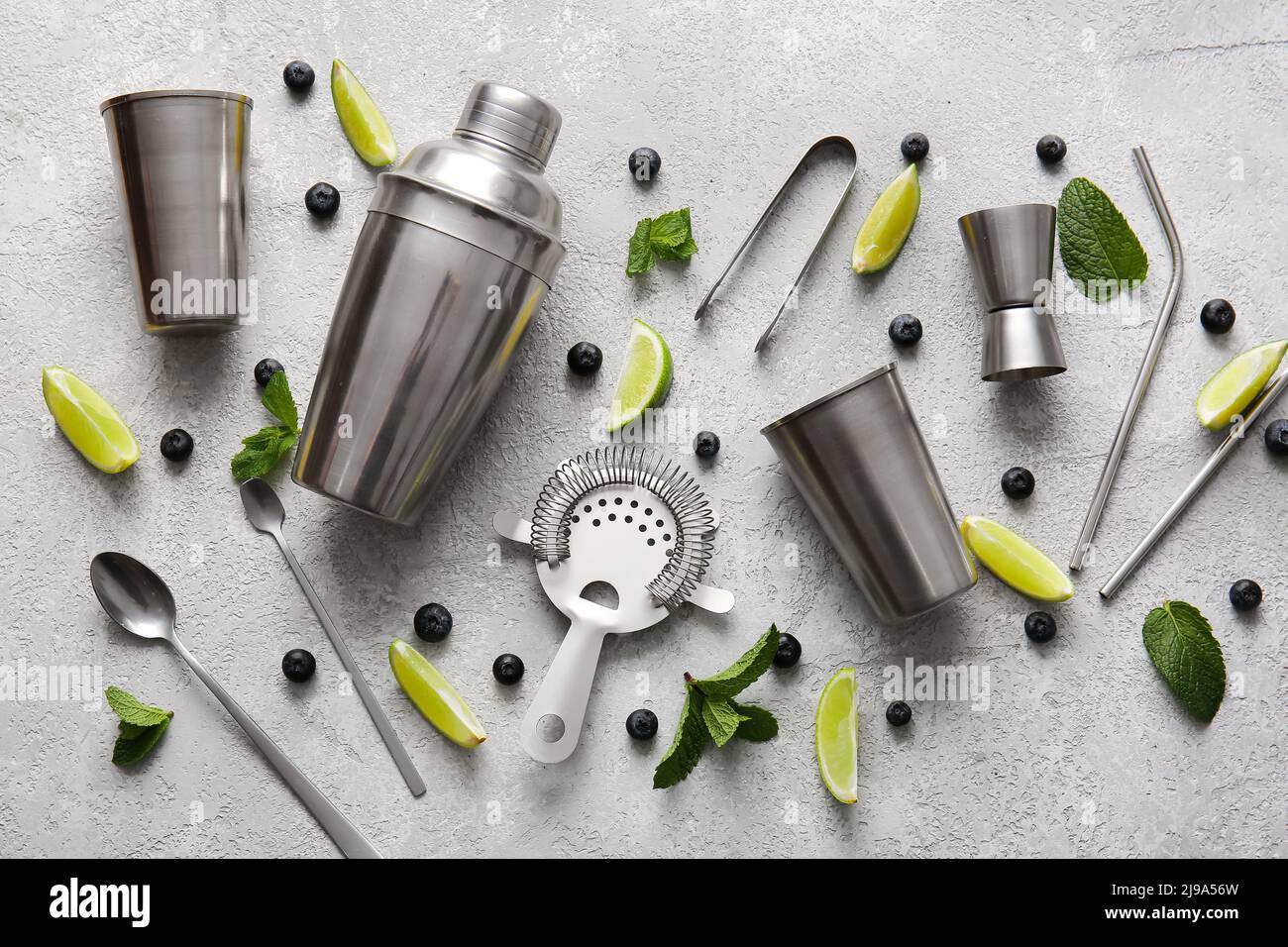 Different bartender tools and cocktail ingredients on grey background