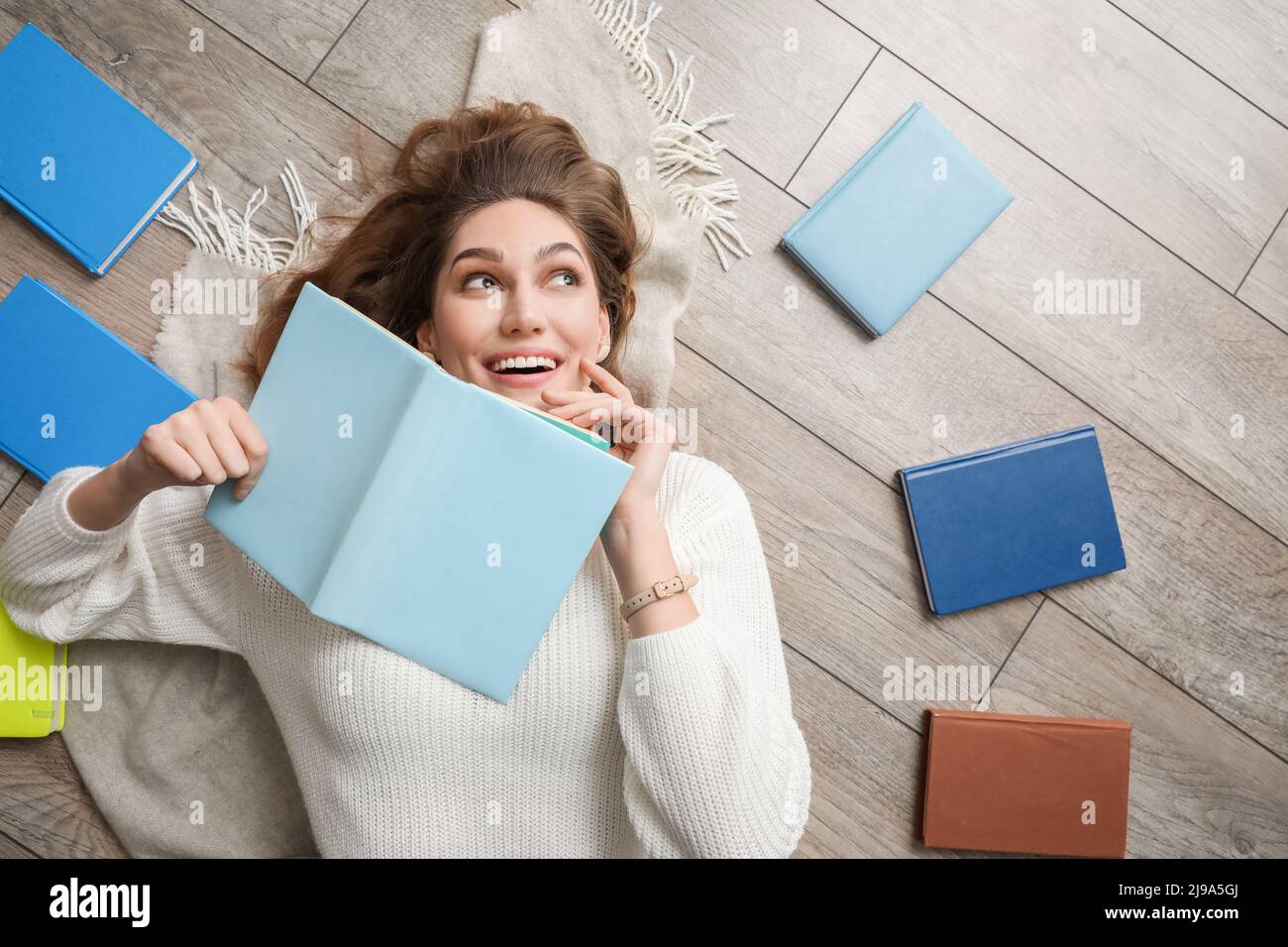 Beautiful happy woman lying on wooden floor with books Stock Photo - Alamy