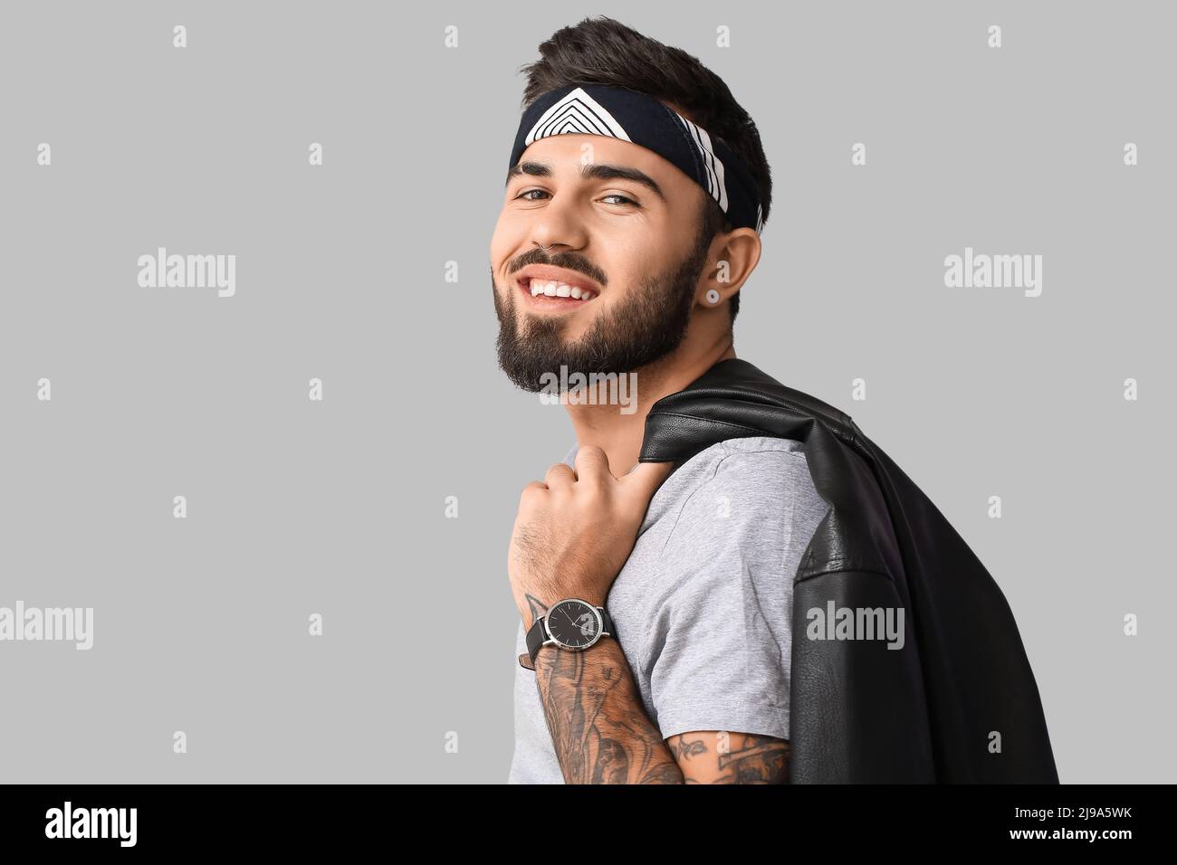 Smiling bearded man holding jacket over shoulder on light background ...