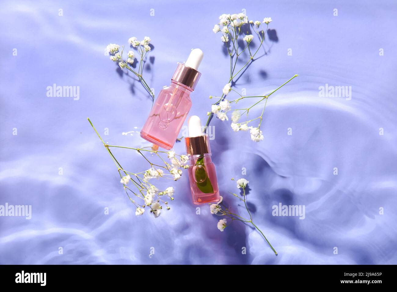 Bottles with natural serum and gypsophila flowers in water on lilac