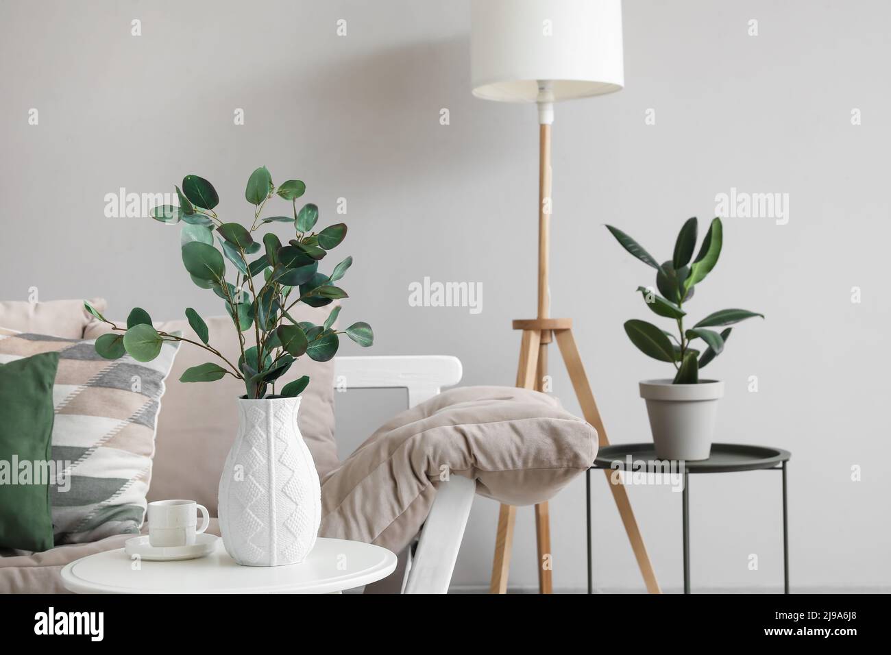 Vase with eucalyptus branches and cup of coffee on table near couch in