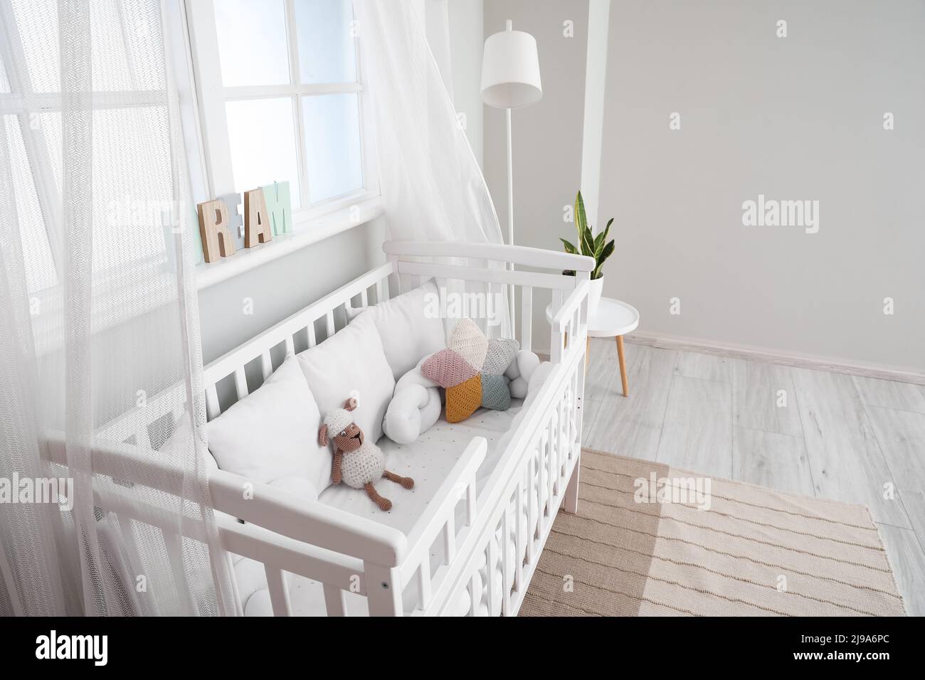 Interior of light nursery with baby crib, lamp and window Stock Photo