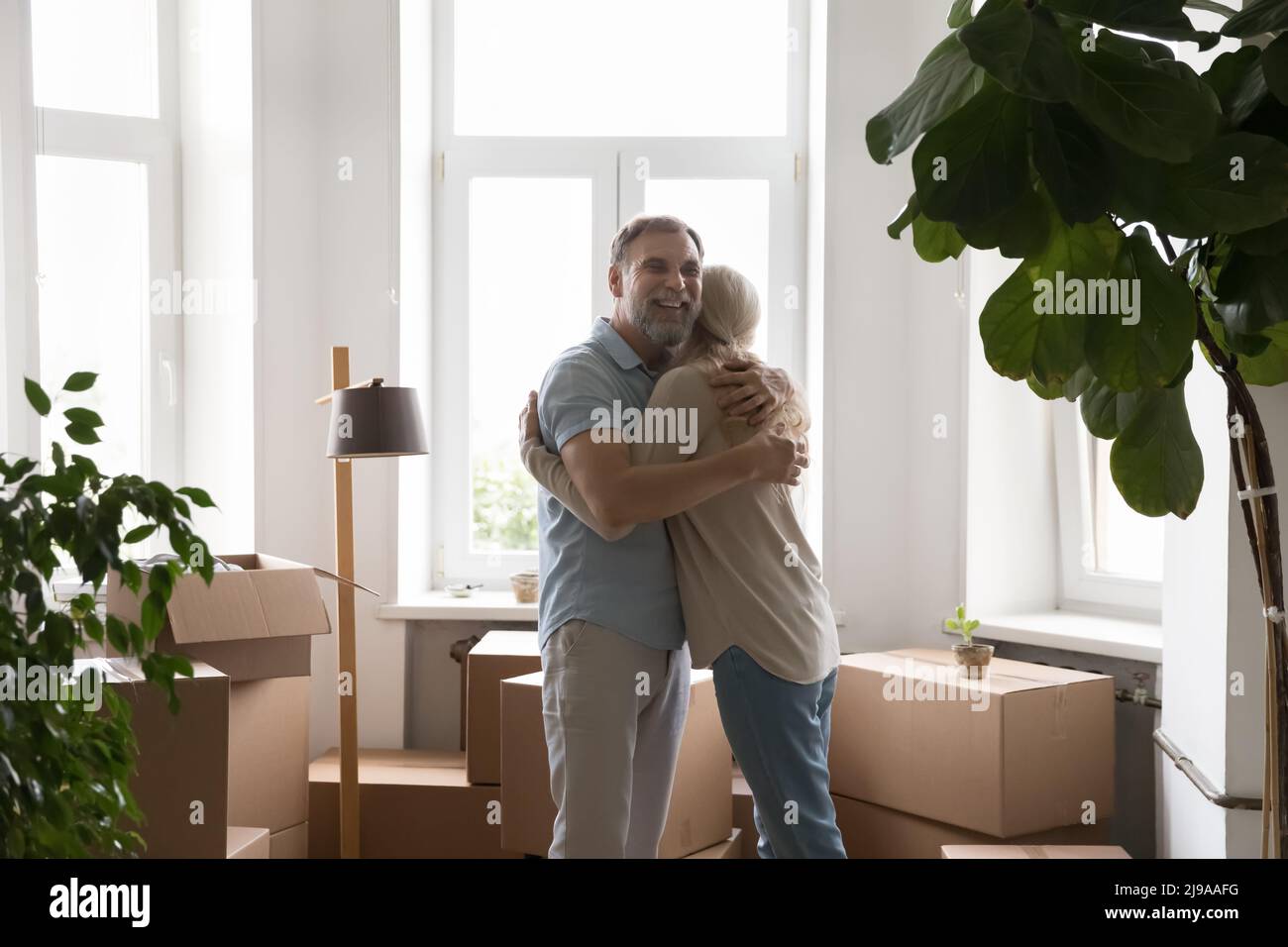 Happy married couple hugging at paper boxes at new home Stock Photo