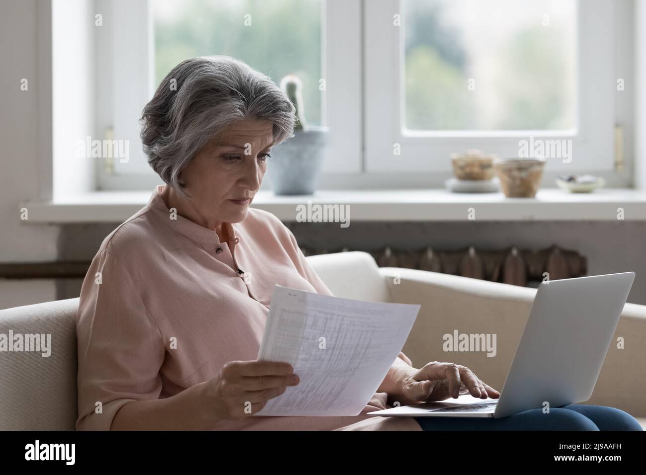 Serious mature accountant woman checking papers for payment at laptop Stock Photo