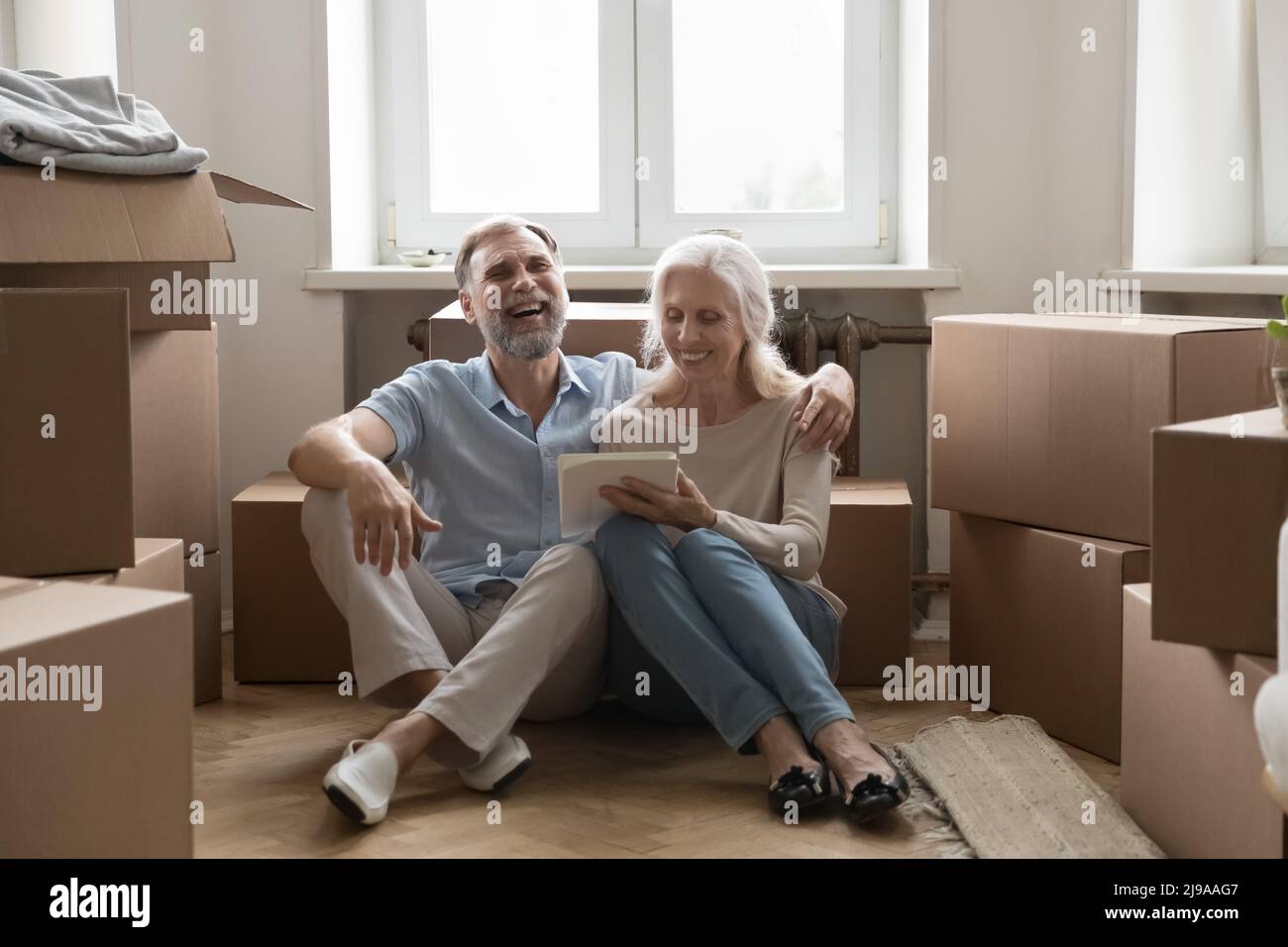 Happy elder 60s married couple using tablet at moving boxes Stock Photo