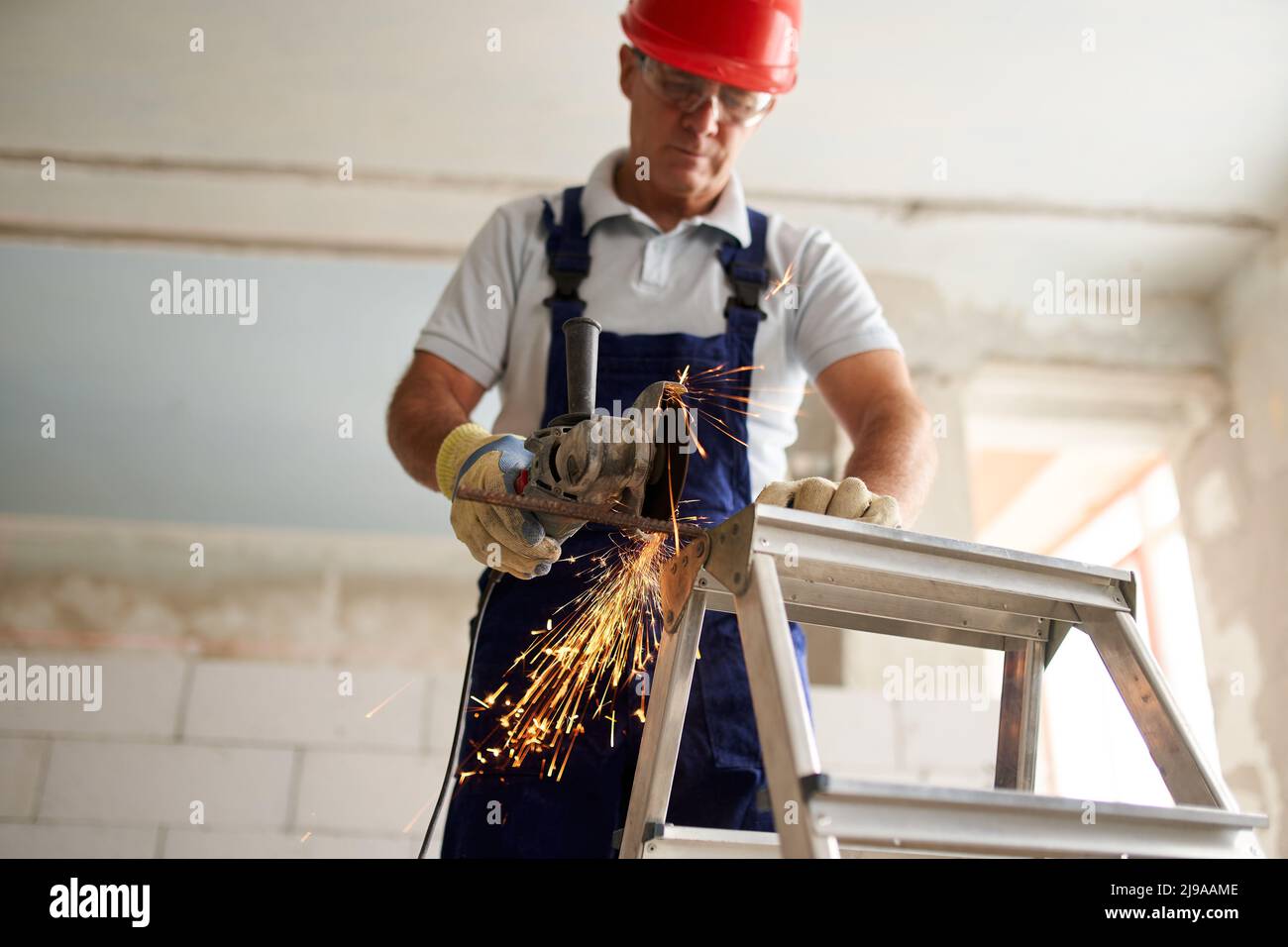 Professional construction worker hands in work gloves using angle grinder to cut metal rod at building site. Close up shot of contractor cutting iron Stock Photo
