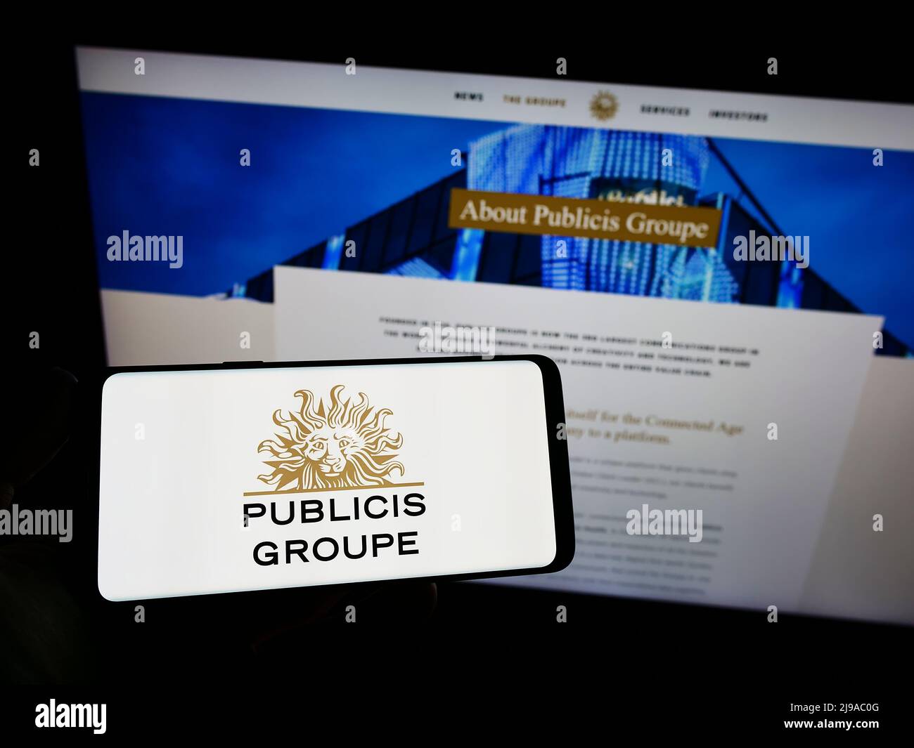 Person holding smartphone with logo of French advertising company Publicis Groupe S.A. on screen in front of website. Focus on phone display. Stock Photo