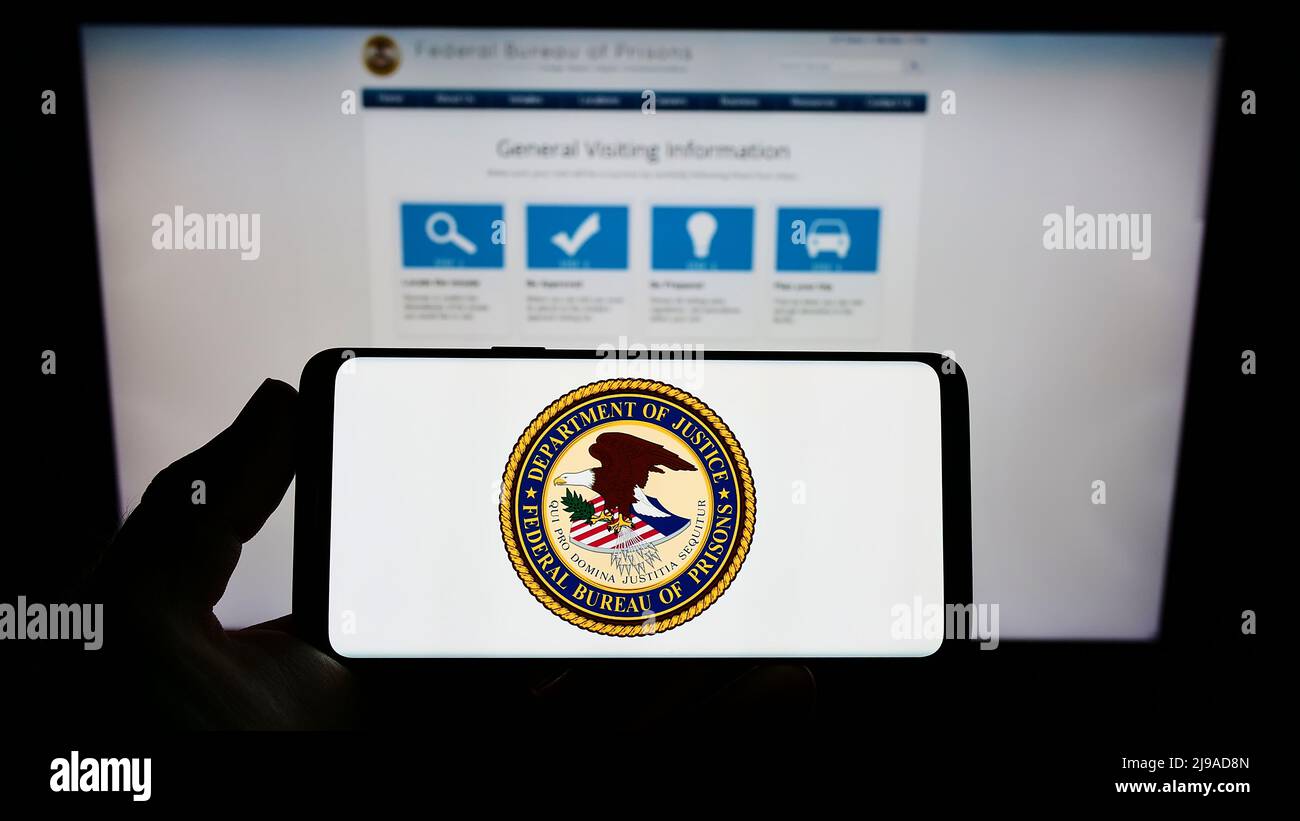 Person holding smartphone with seal of US agency Federal Bureau of Prisons (BOP) on screen in front of website. Focus on phone display. Stock Photo