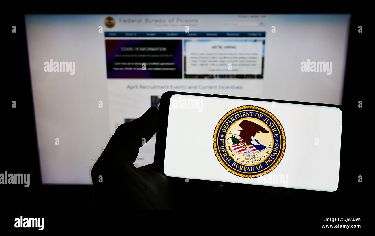 Person holding cellphone with seal of American agency Federal Bureau of Prisons (BOP) on screen in front of webpage. Focus on phone display. Stock Photo