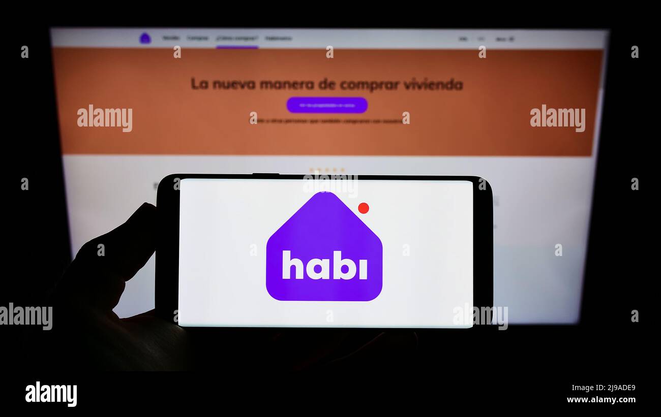 Person holding cellphone with logo of Colombian company INVERSIONES MCN S.A.S (Habi) on screen in front of webpage. Focus on phone display. Stock Photo