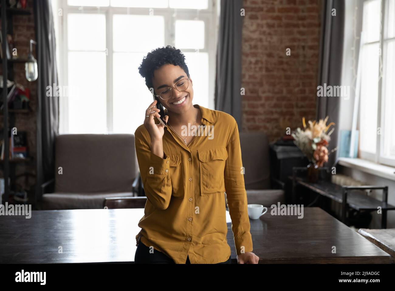 African woman standing indoor holds smartphone lead pleasant conversation Stock Photo