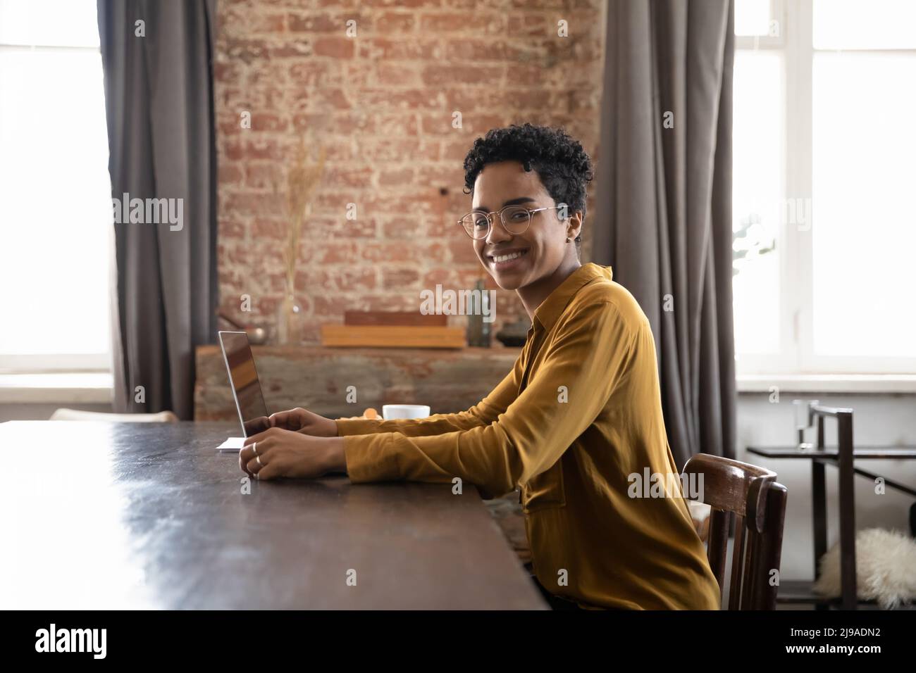 African woman sit at desk with laptop looks at camera Stock Photo