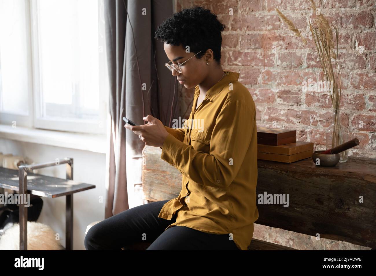 Serious African curly haired woman sit indoors with smartphone Stock Photo