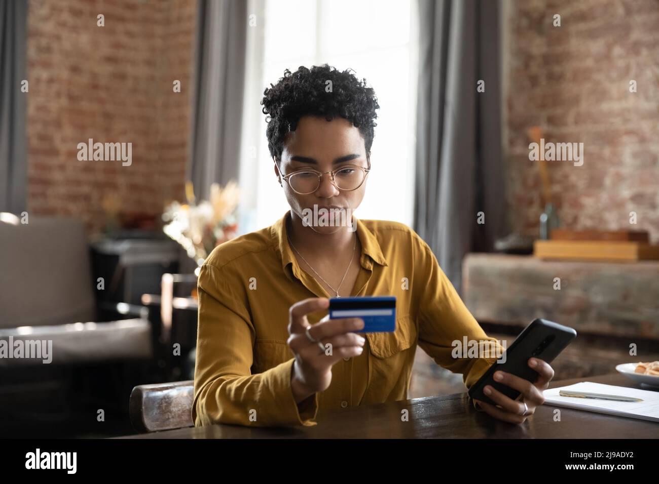 Serious African woman makes money transfer use smartphone and card Stock Photo