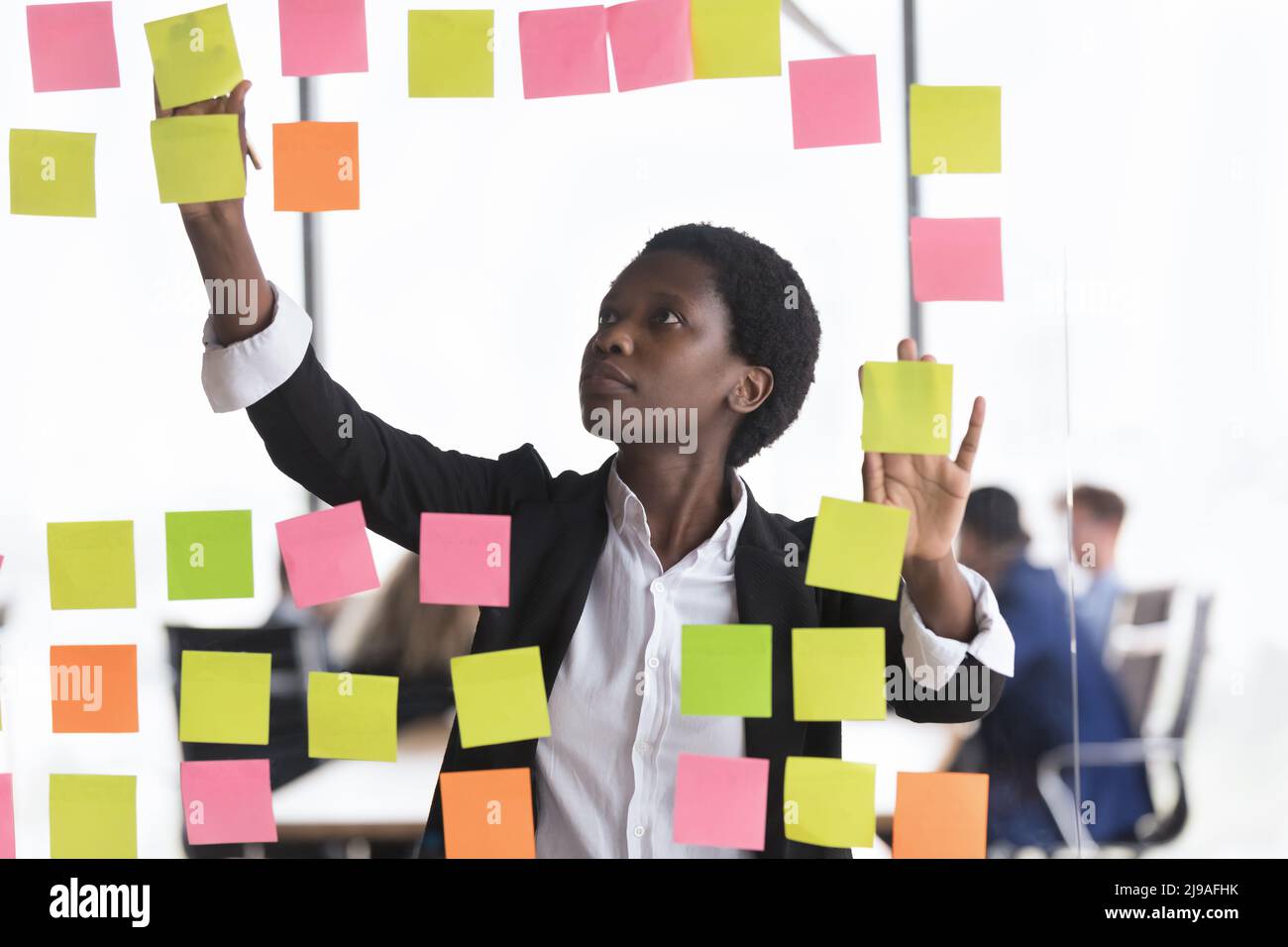 African businesslady jotting on adhesive stickers attached on glass wall Stock Photo