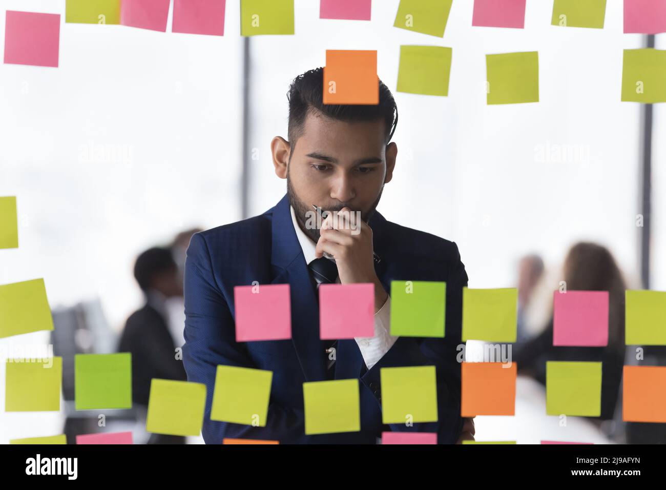 Thoughtful Indian businessman reviewing notes written on post-it stickers Stock Photo