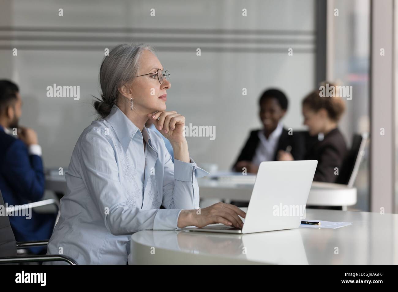 Thoughtful aged businesswoman sit at desk looks into distance Stock Photo