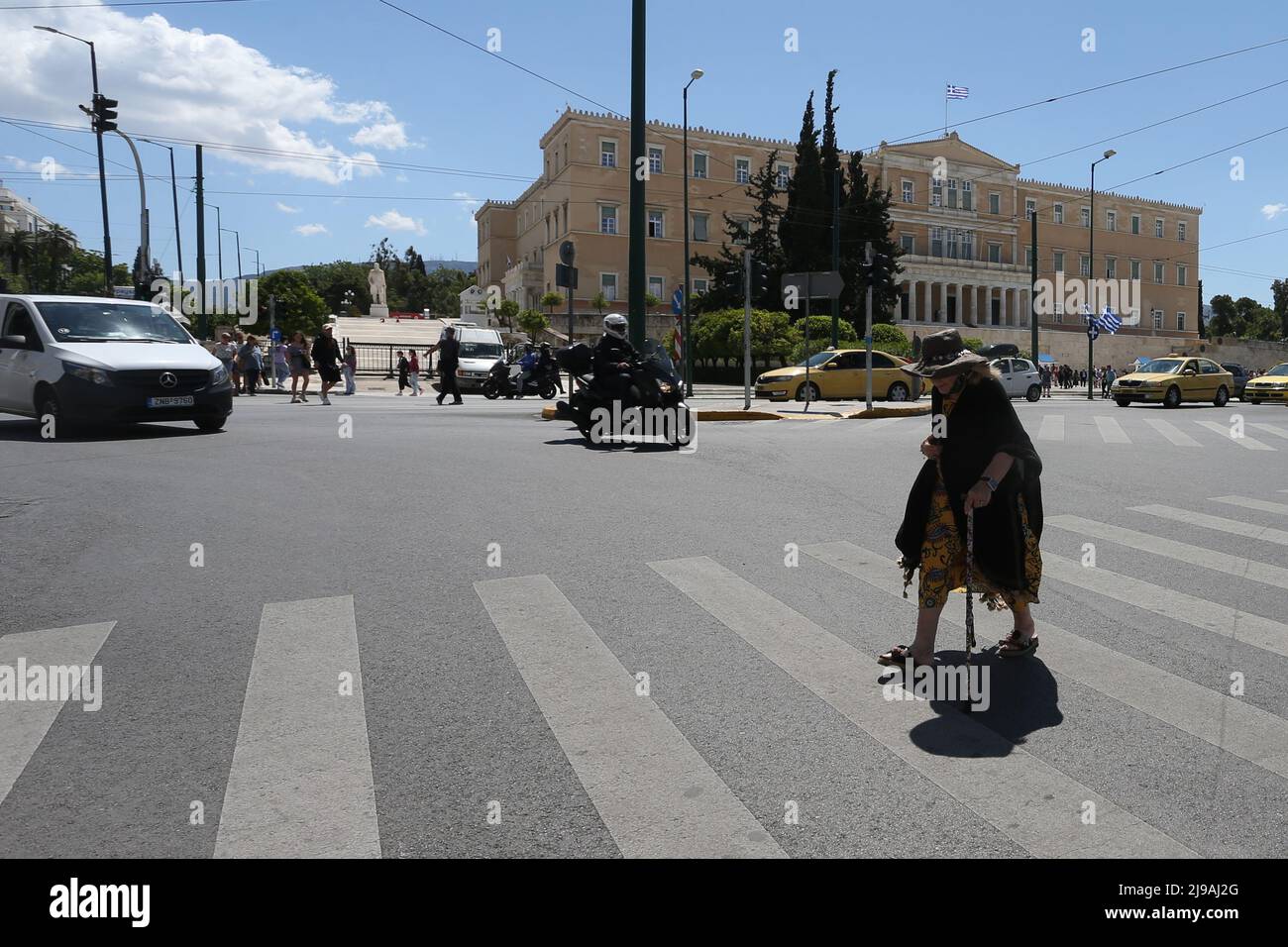 An elderly woman with a cane crosses the street in the center of Athens