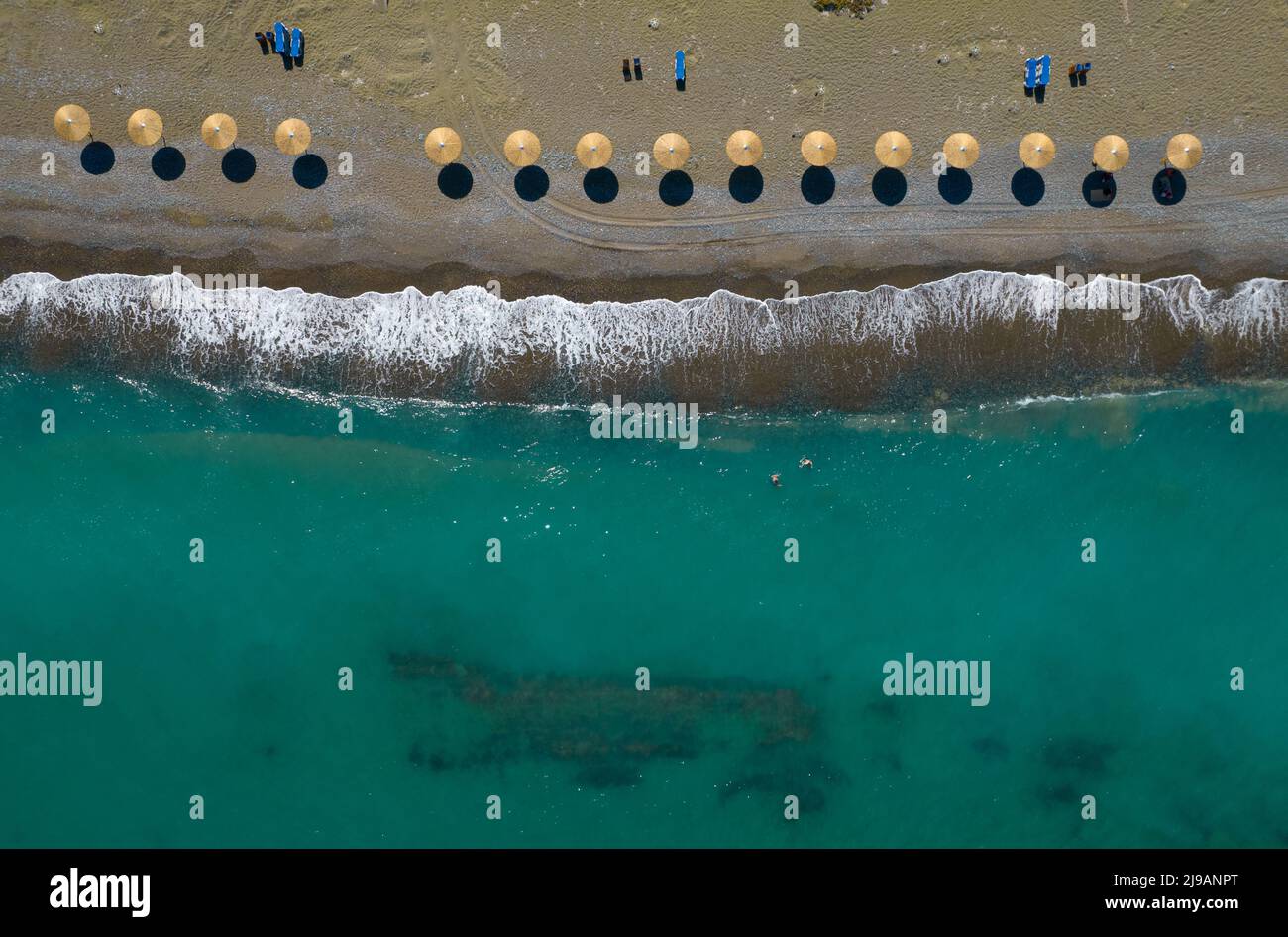 Aerial view from a flying drone of beach umbrellas in a row on an empty beach with breaking waves. Summer holidays Paphos Cyprus Stock Photo