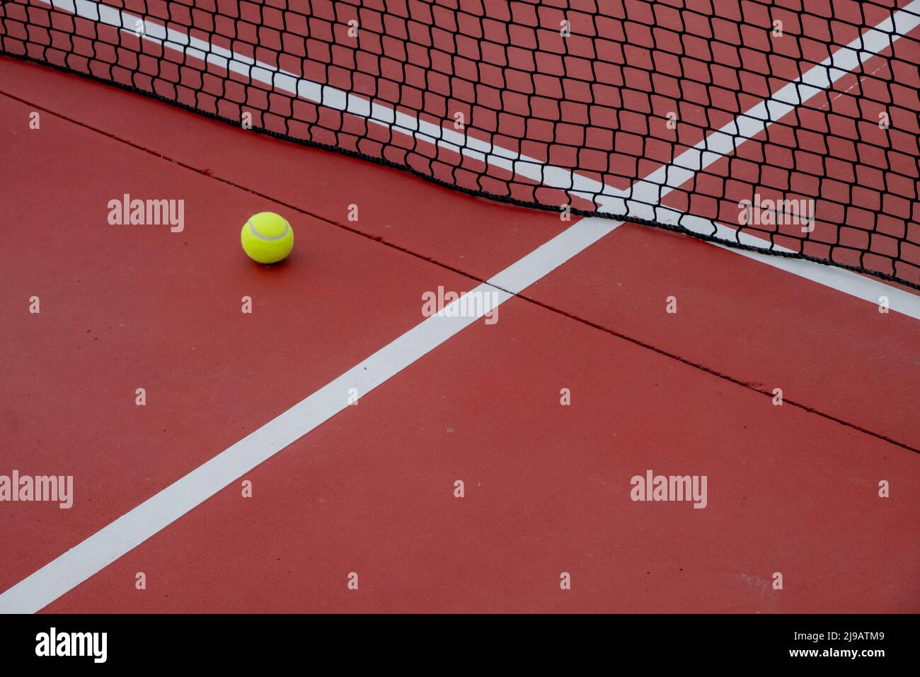 Tennis ball next to the net of a red hard surface tennis court Stock