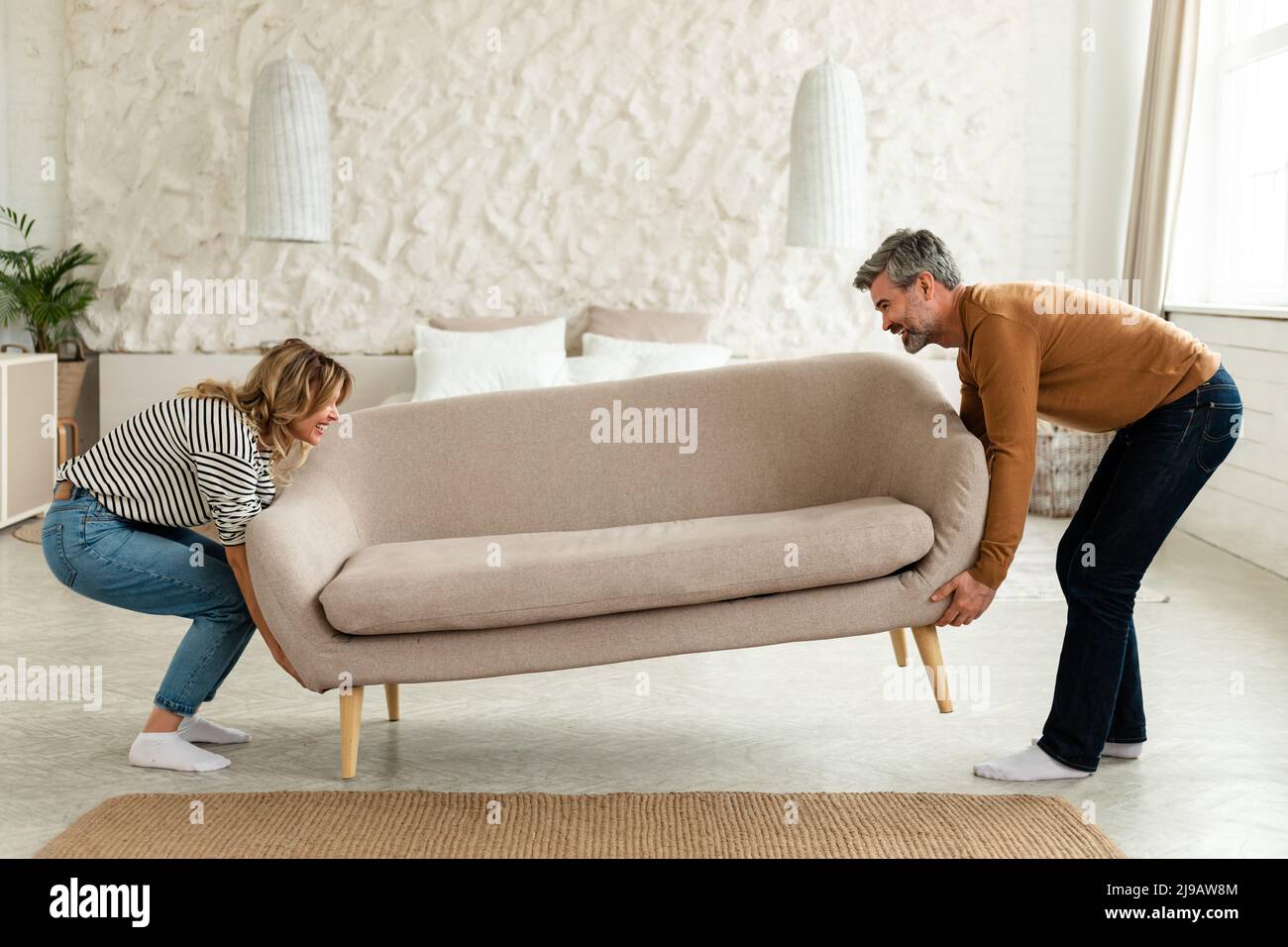 Happy Couple Putting Sofa Together After Renovation At Home Stock Photo