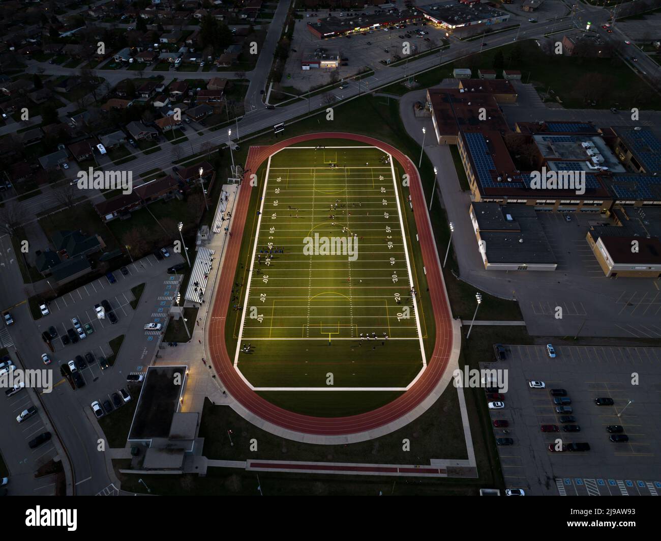 An aerial view above a new, municipal, small city football field is seen illuminated at night, as a game is being played. Stock Photo
