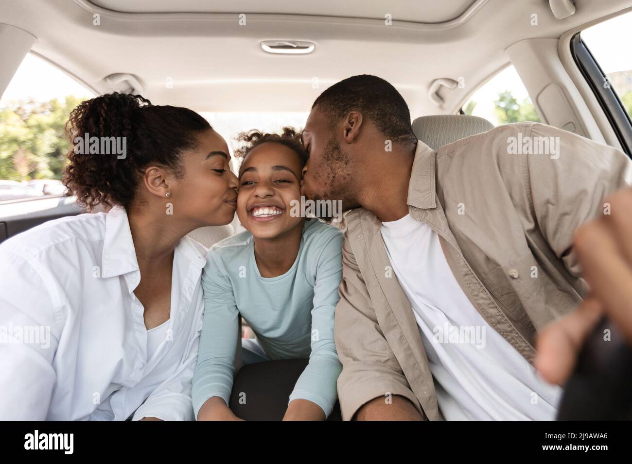 Cheerful Black Parents Kissing Daughter Sitting In New Car Stock Photo