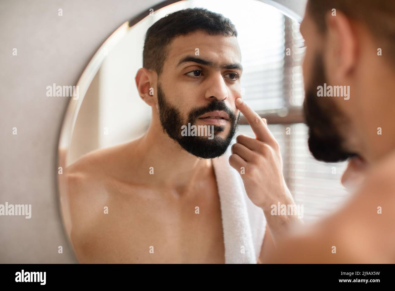 Guy looking in the mirror applying cream on face Stock Photo
