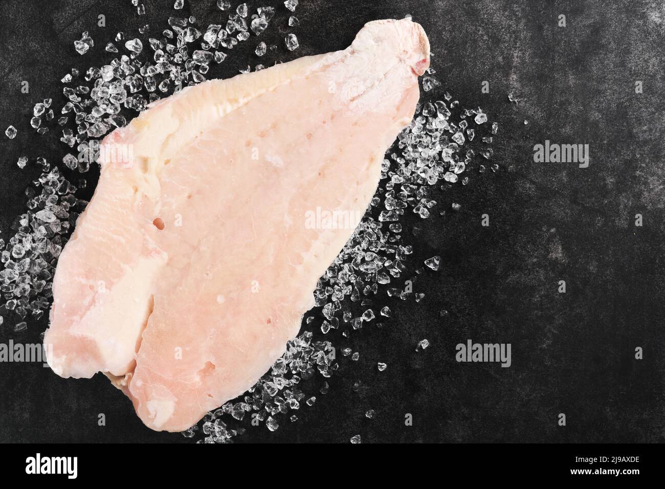 Pangasius frozen fillet. Raw fillet of white fish catfish. Pangasius with spices. Black background. Top view. Stock Photo