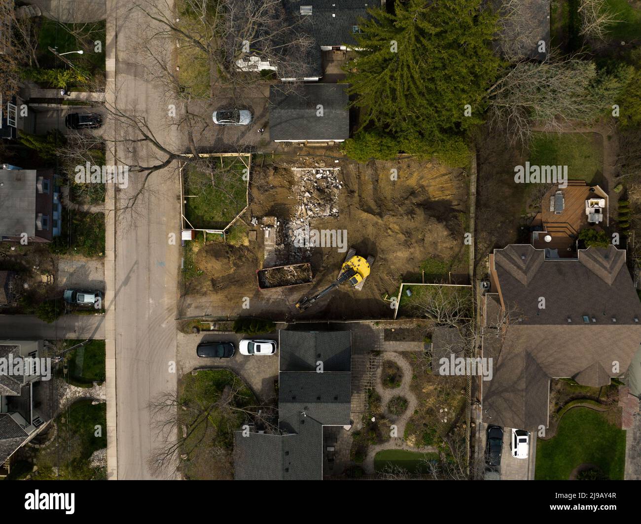 An aerial view above a home in a neighbourhood being torn down, demolished by an excavator during the day. Stock Photo