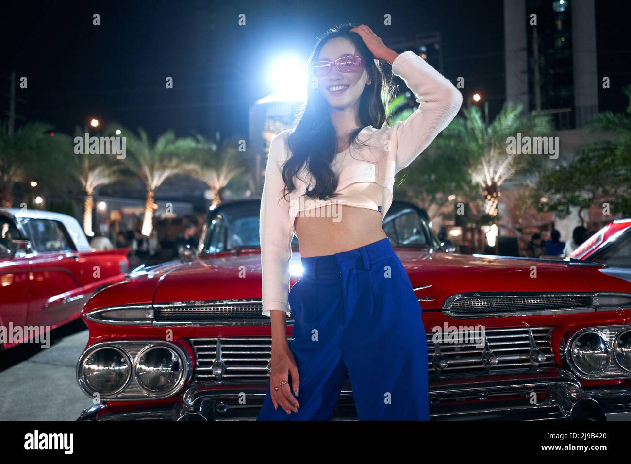 Sensual asian woman posing in front of a luxury antique car in a night fair Stock Photo