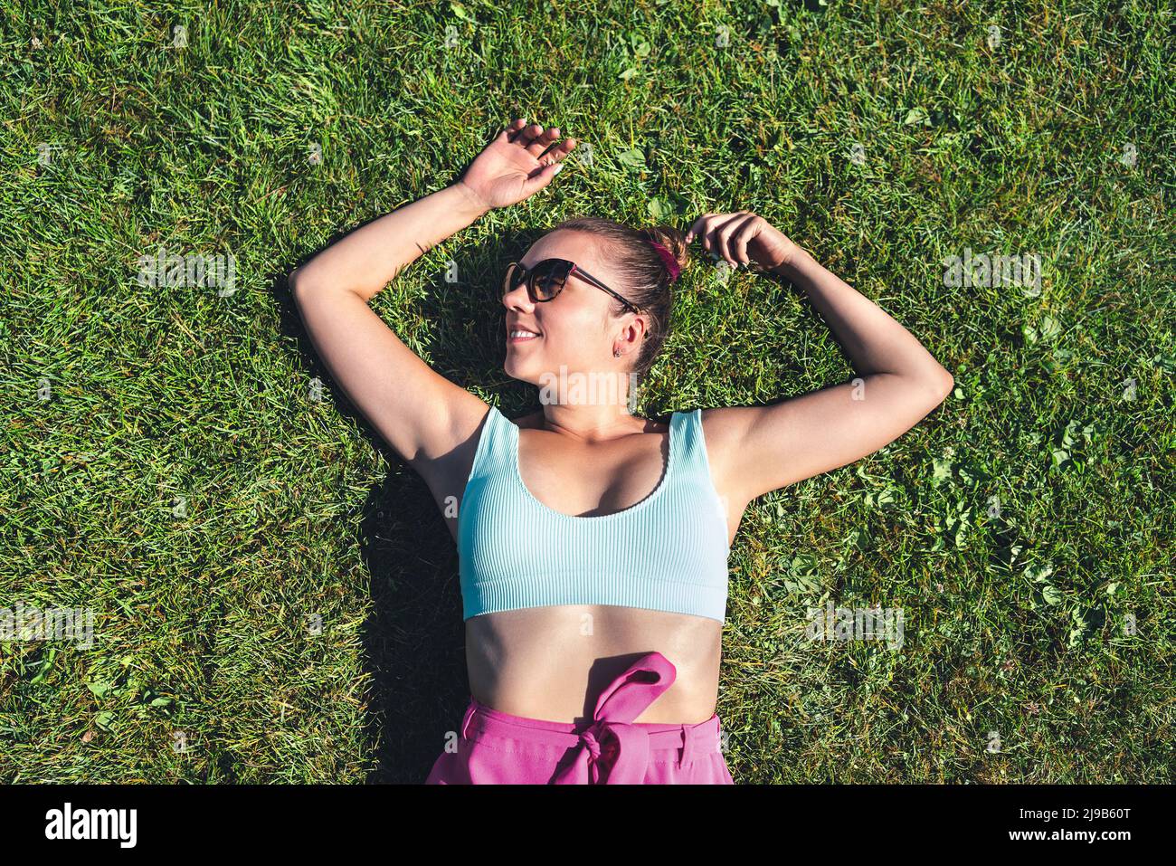 Resting in grass in green garden, above top view. Woman lying down relaxing in the nature. Lazy girl day dreaming outside in the park. Stock Photo